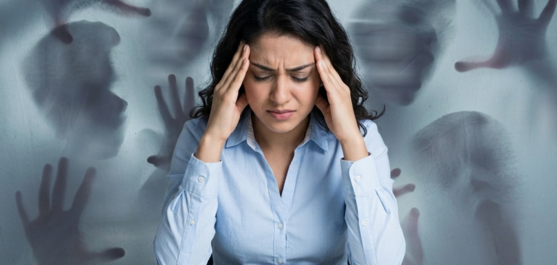 Woman experiencing psychological distress with blurred figures in the background representing symptoms of untreated mental health conditions.