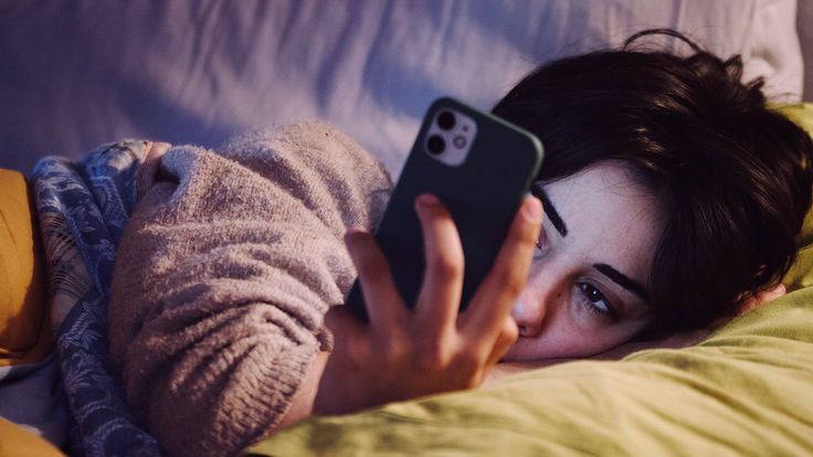 Woman scrolling phone in bed at night, a common cause of insomnia and sleep disorders treated in Nagpur